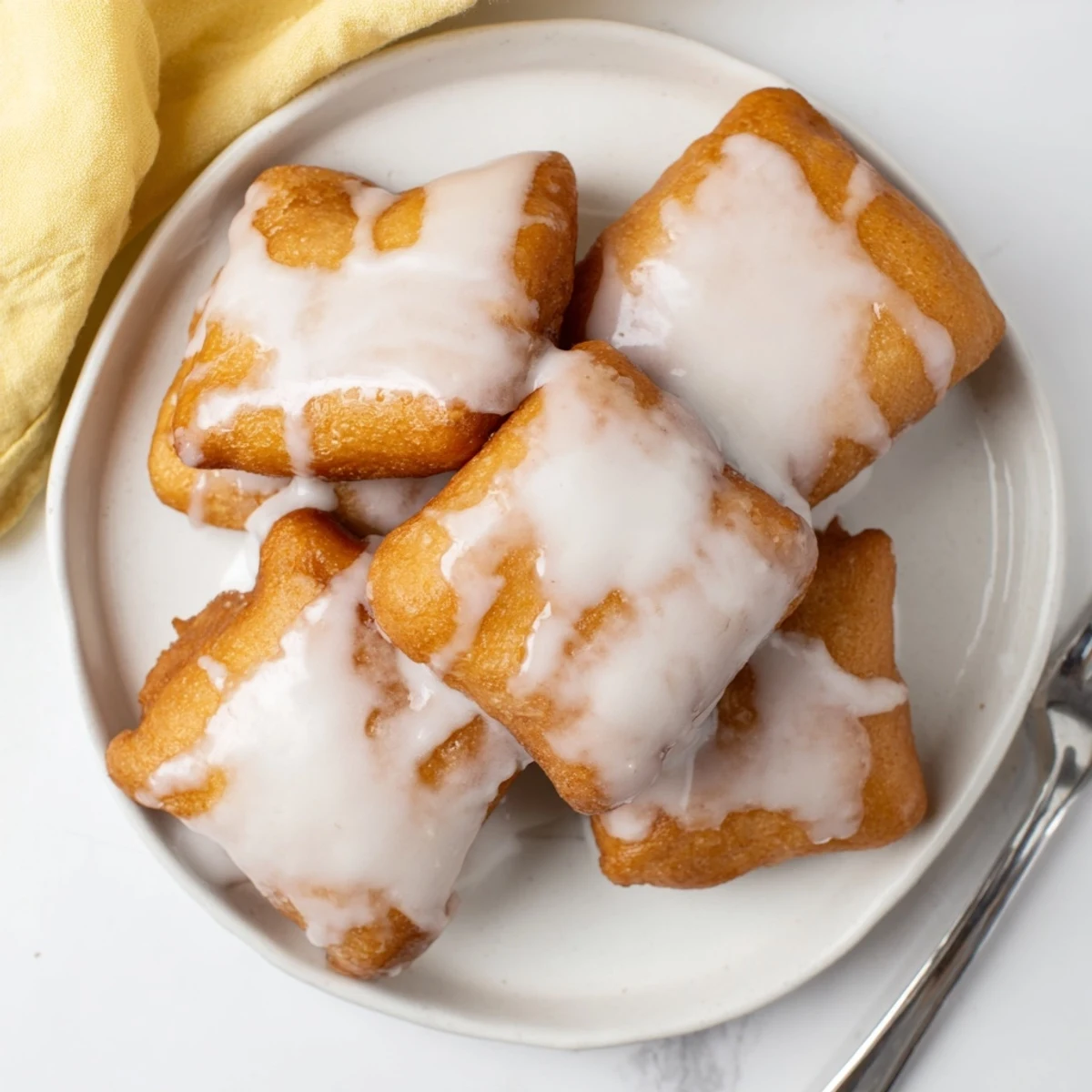 Stack of fluffy glazed buttermilk beignet squares dripping with sweet vanilla glaze topping