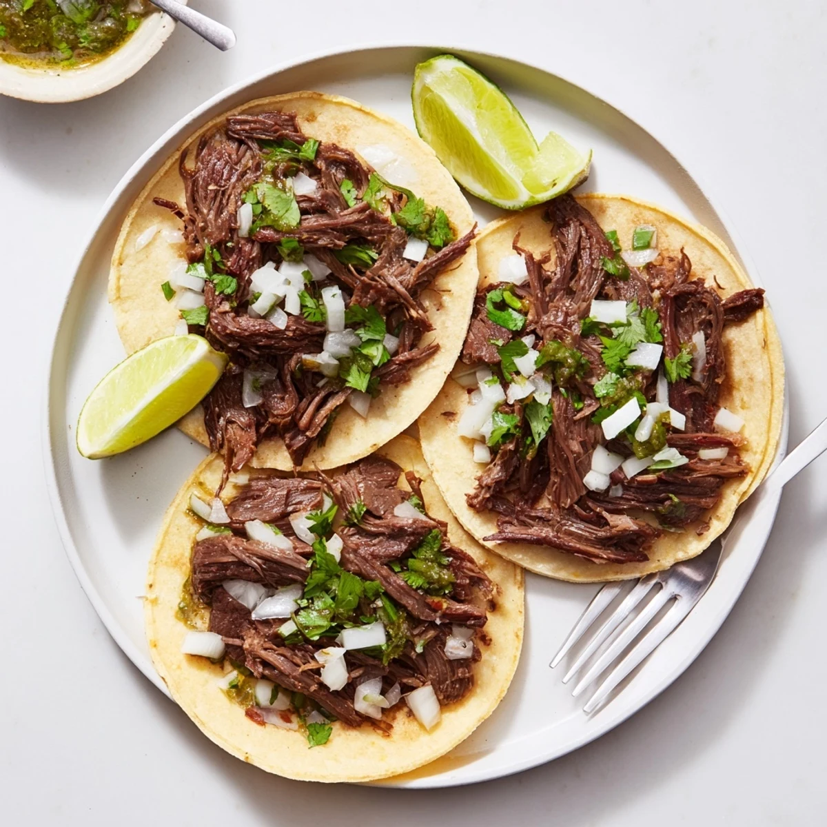 Slow-cooked beef cheek tacos with shredded meat piled in warm corn tortillas topped with fresh cilantro, onion, and zesty salsa