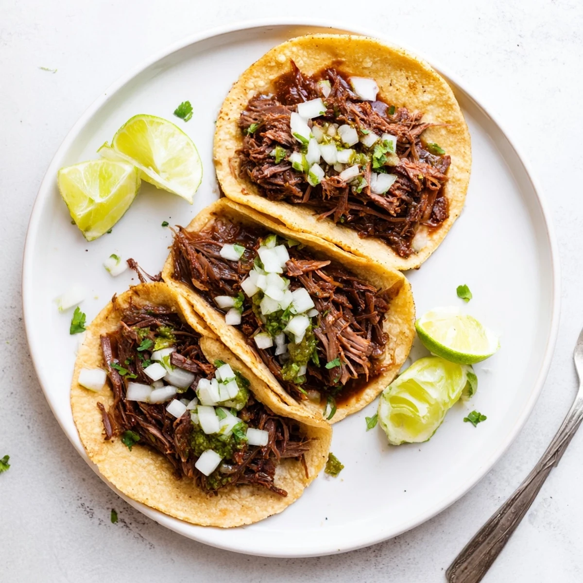 Tender braised beef cheek tacos served on soft corn tortillas with vibrant garnishes of white onion, chopped cilantro, and lime wedges