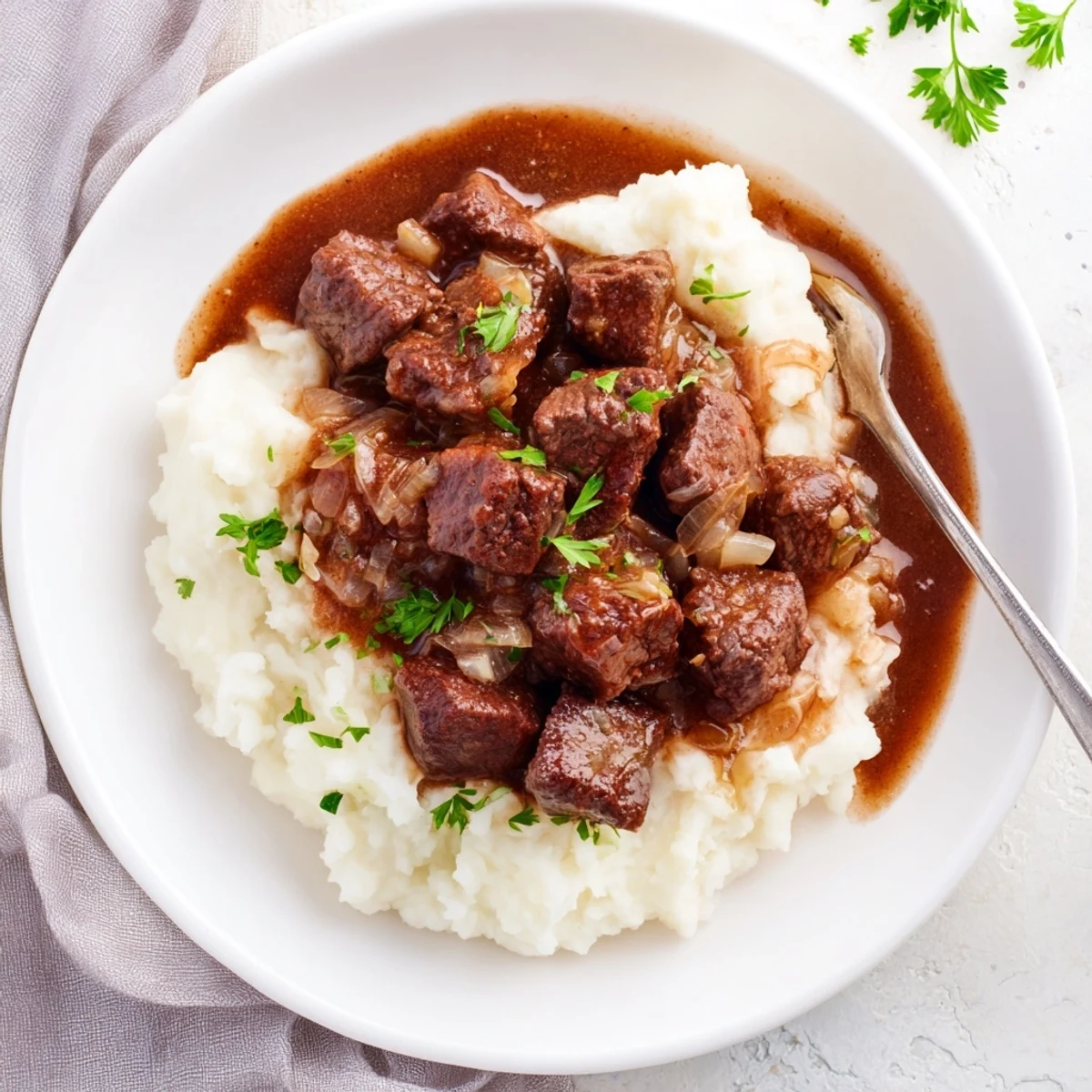 Slow cooker beef tips and gravy served over fluffy mashed potatoes with chopped parsley garnish