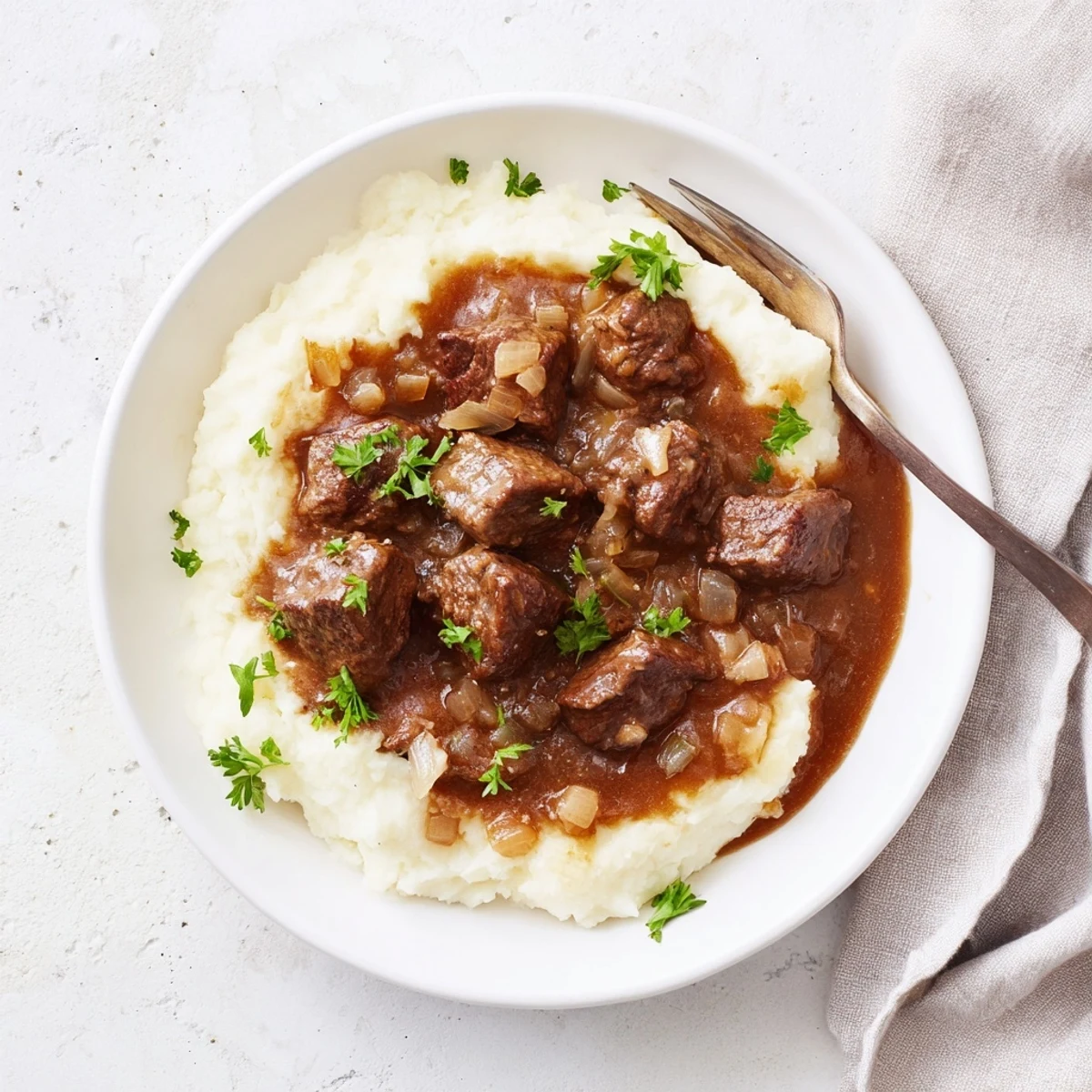 Fork-tender slow cooker beef tips and gravy plated over creamy mashed potatoes with fresh green parsley
