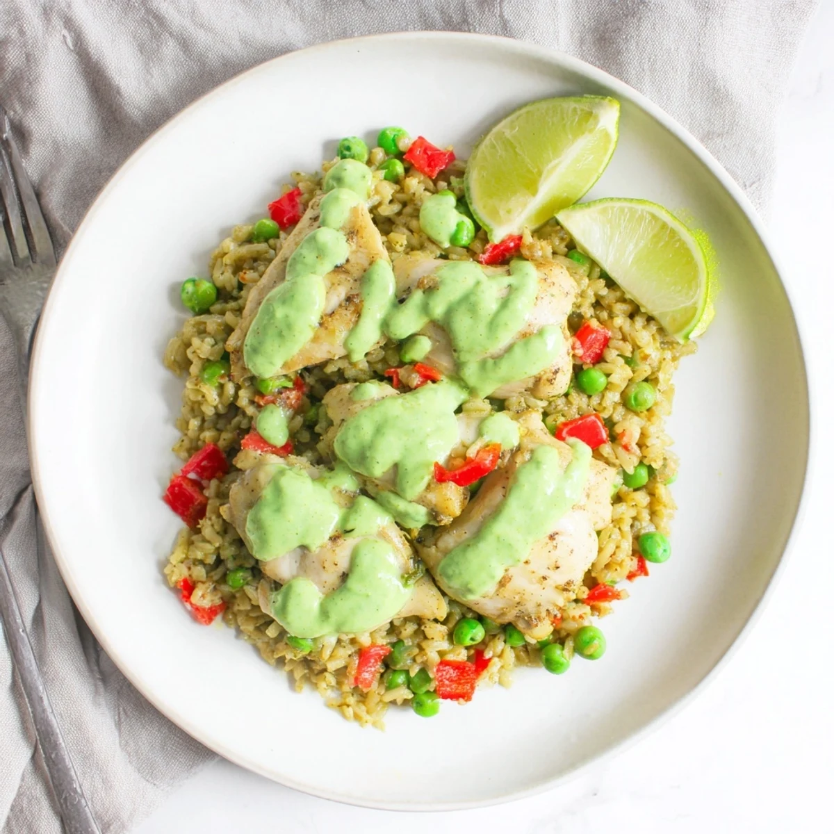 Golden chicken thighs rest atop cilantro-infused rice with vibrant green Peruvian sauce drizzled generously over the top