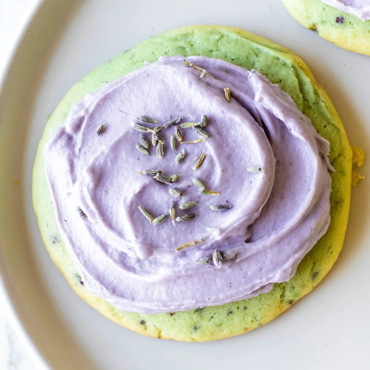 Soft green matcha sugar cookies with swirls of purple lavender frosting on a rustic ceramic plate