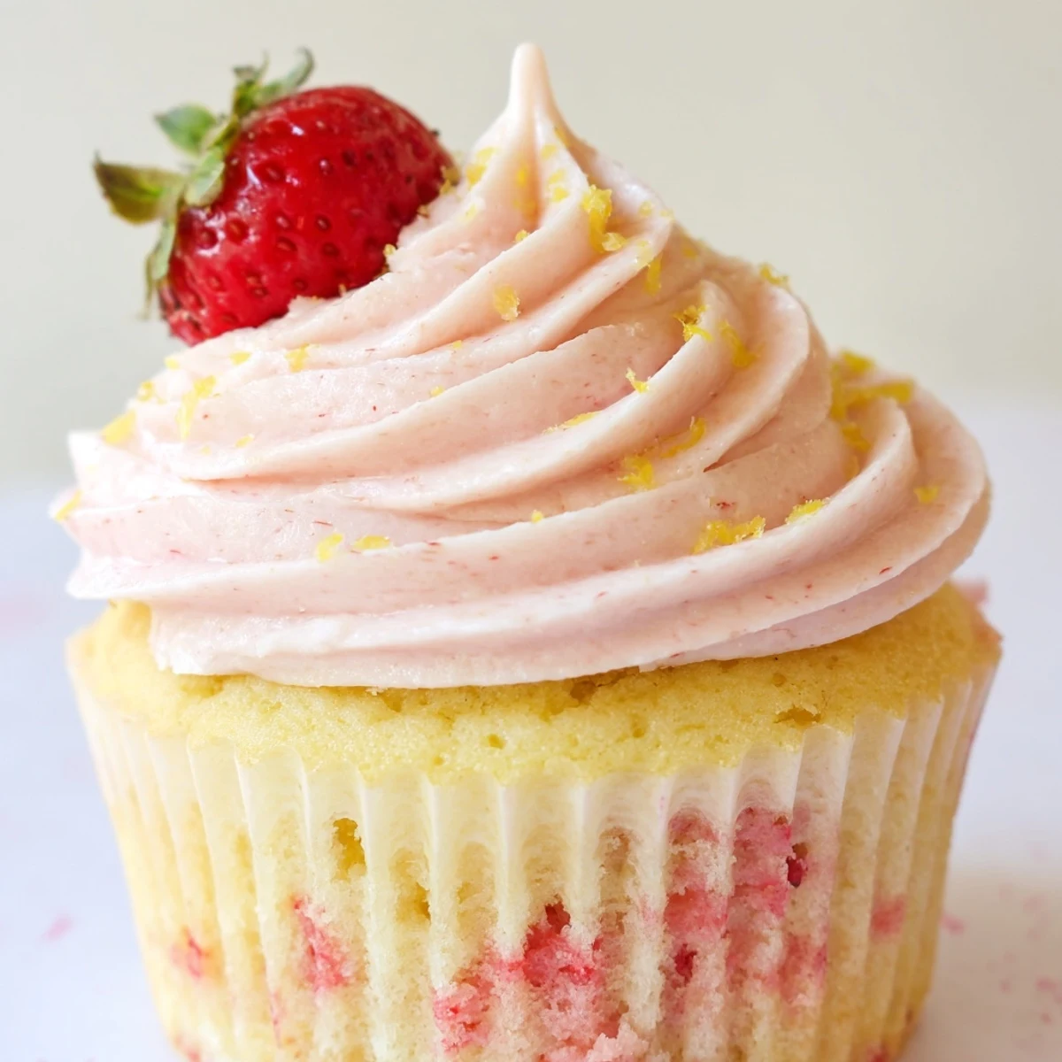 Golden strawberry lemonade cupcakes topped with swirled pink buttercream and lemon zest sprinkles