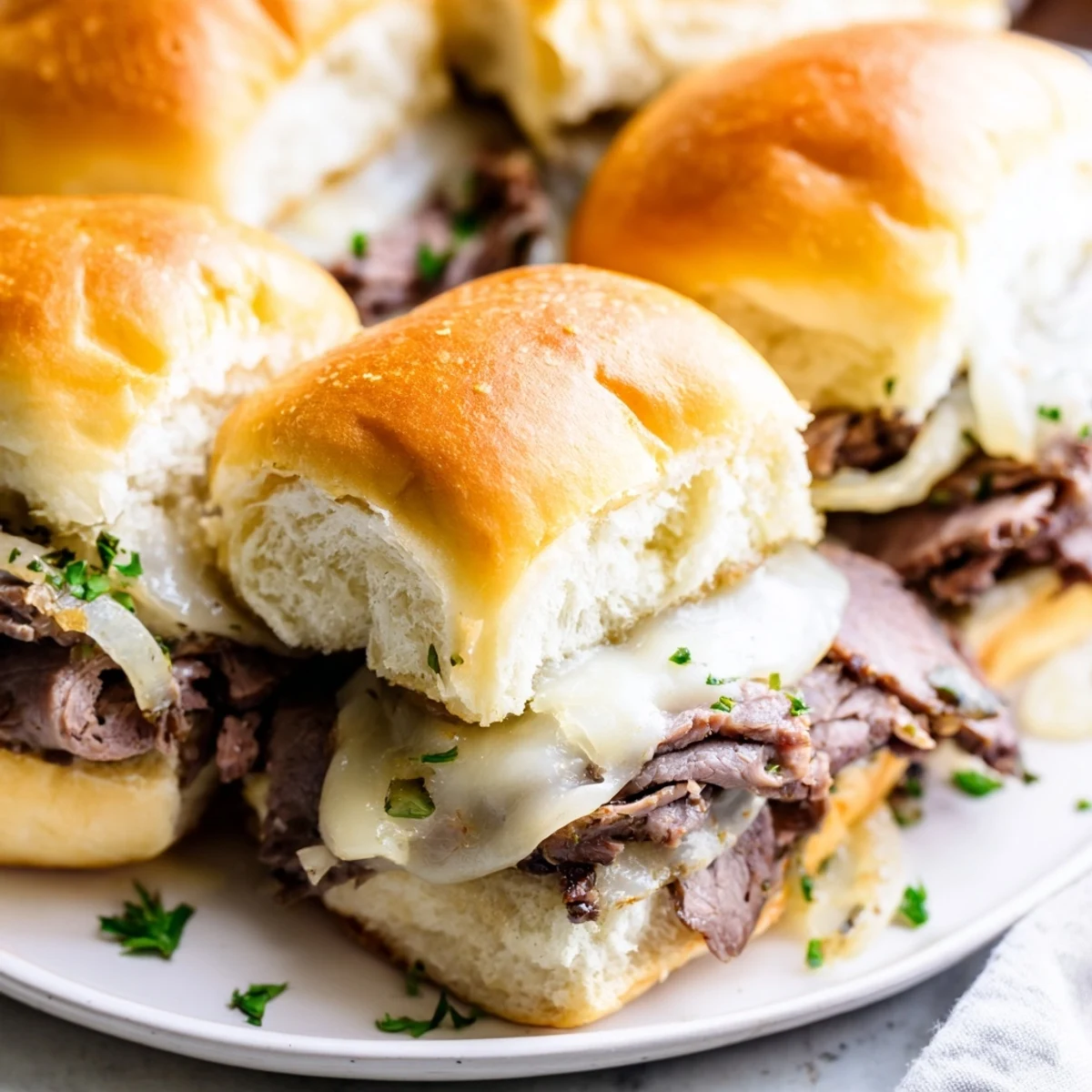 Golden French dip sliders stacked with melted provolone and caramelized onions on toasted brioche rolls