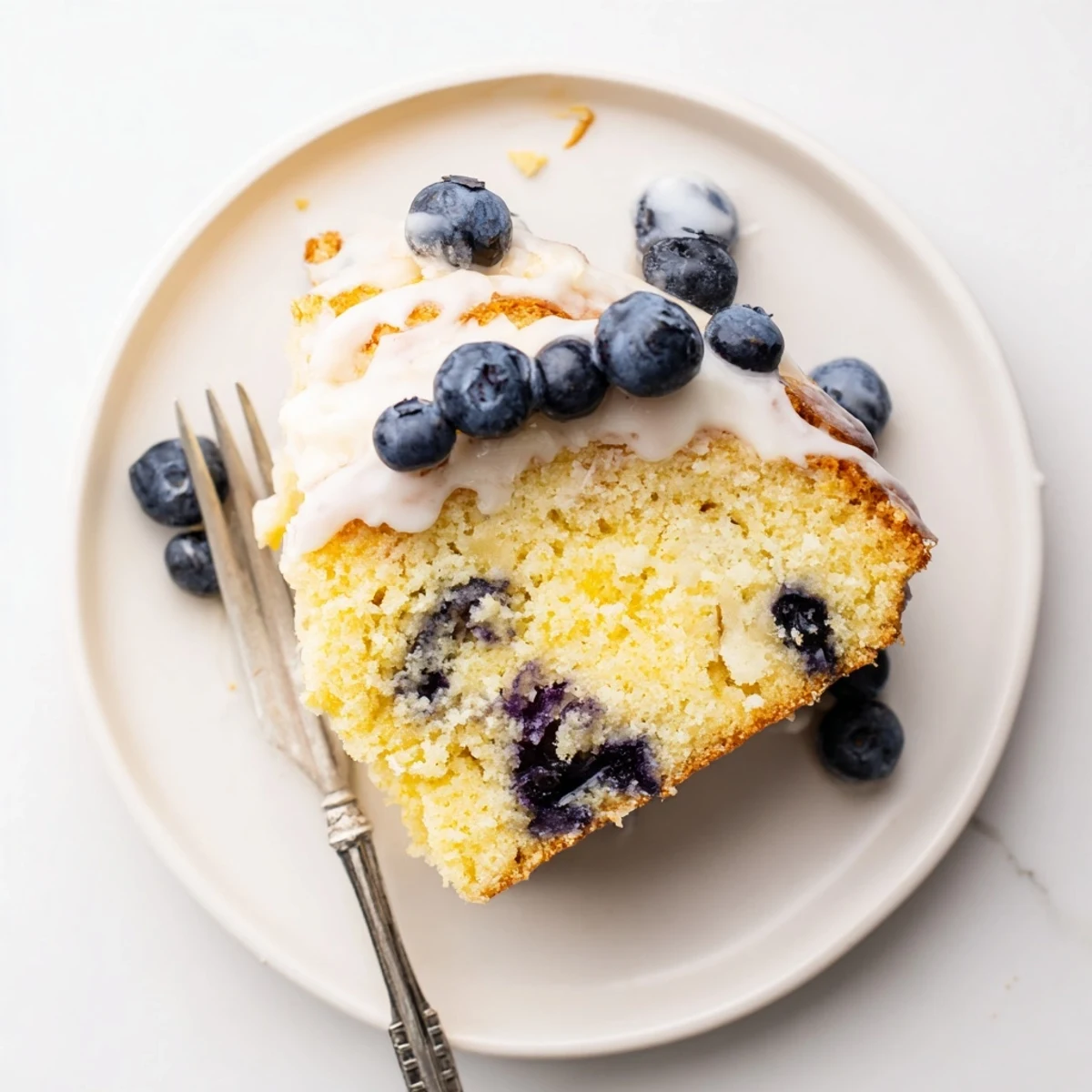 Golden slice of lemon blueberry cake topped with fresh berries and powdered sugar
