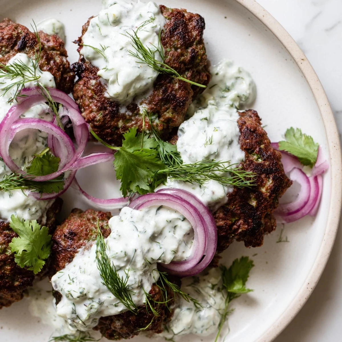 Hand-shaped smashed beef kebabs garnished with fresh herbs and tangy cucumber yogurt dip