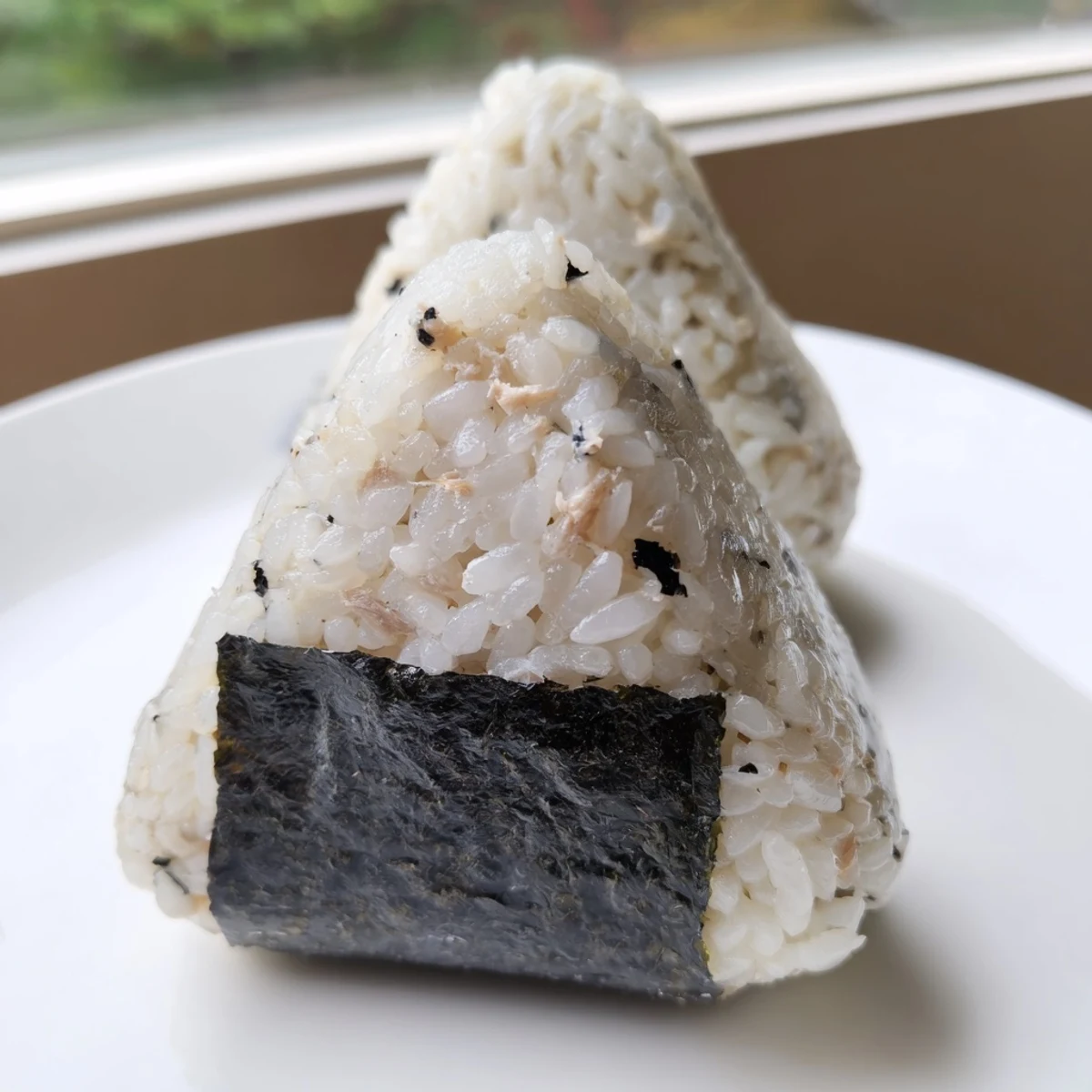 Handheld Japanese tuna mayo onigiri featuring fluffy rice filled with savory creamy tuna mixture