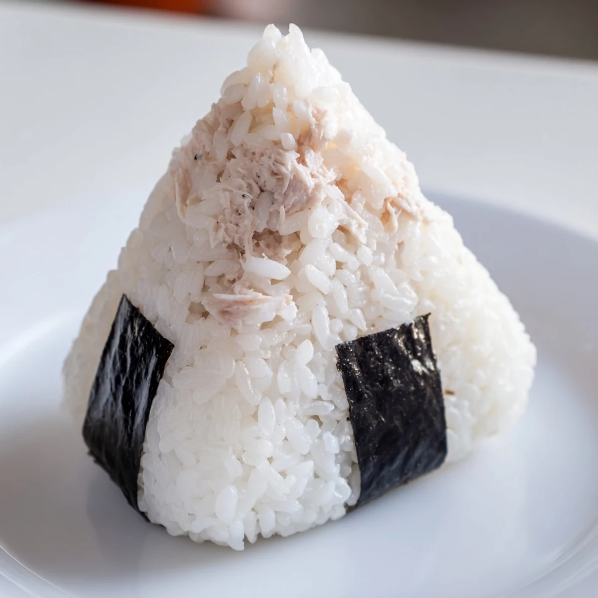 Triangle-shaped tuna mayo onigiri with dark nori accents on a clean white plate