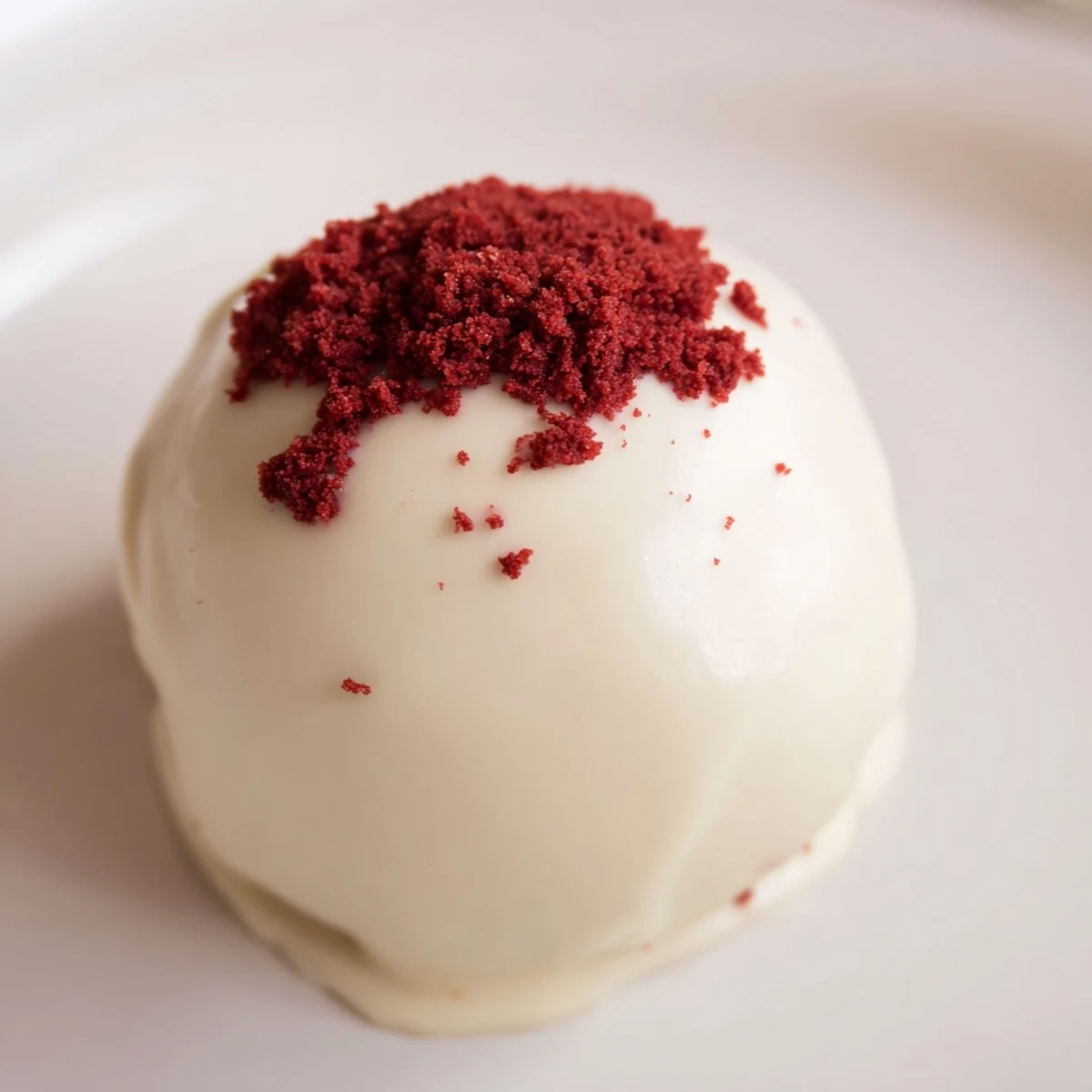 Creamy red velvet cheesecake balls on a white platter with cake crumb garnish