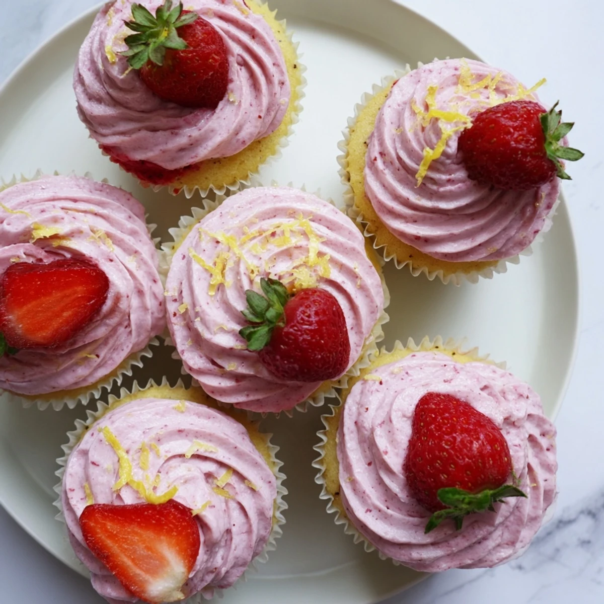 Fresh strawberry lemonade cupcakes with pink strawberry frosting topped with lemon zest garnish