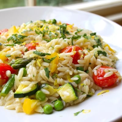 Bright Orzo Primavera served in a white bowl with lemon zest.
